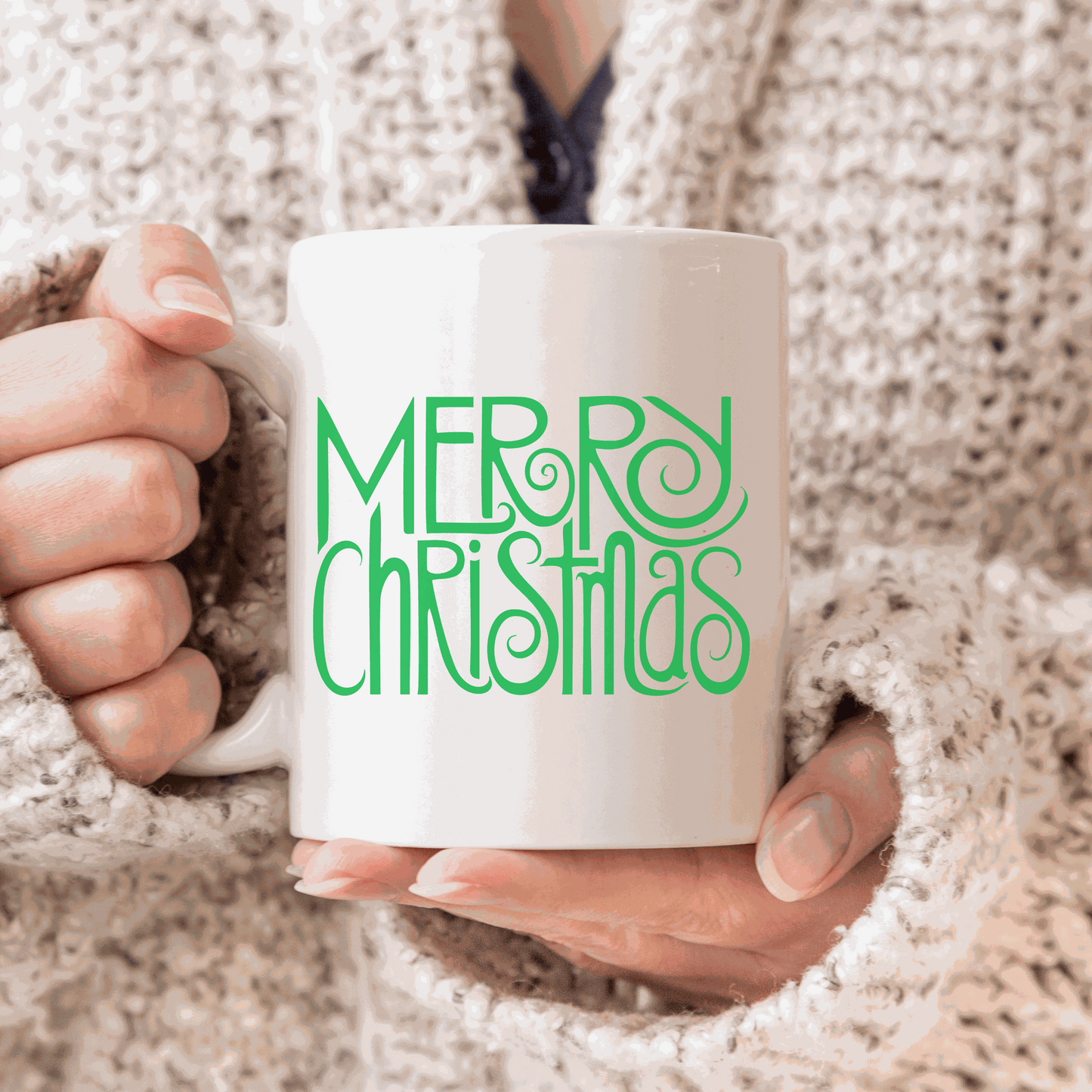Merry Christmas ceramic mug with green festive text design, held by a person in a cozy sweater.
