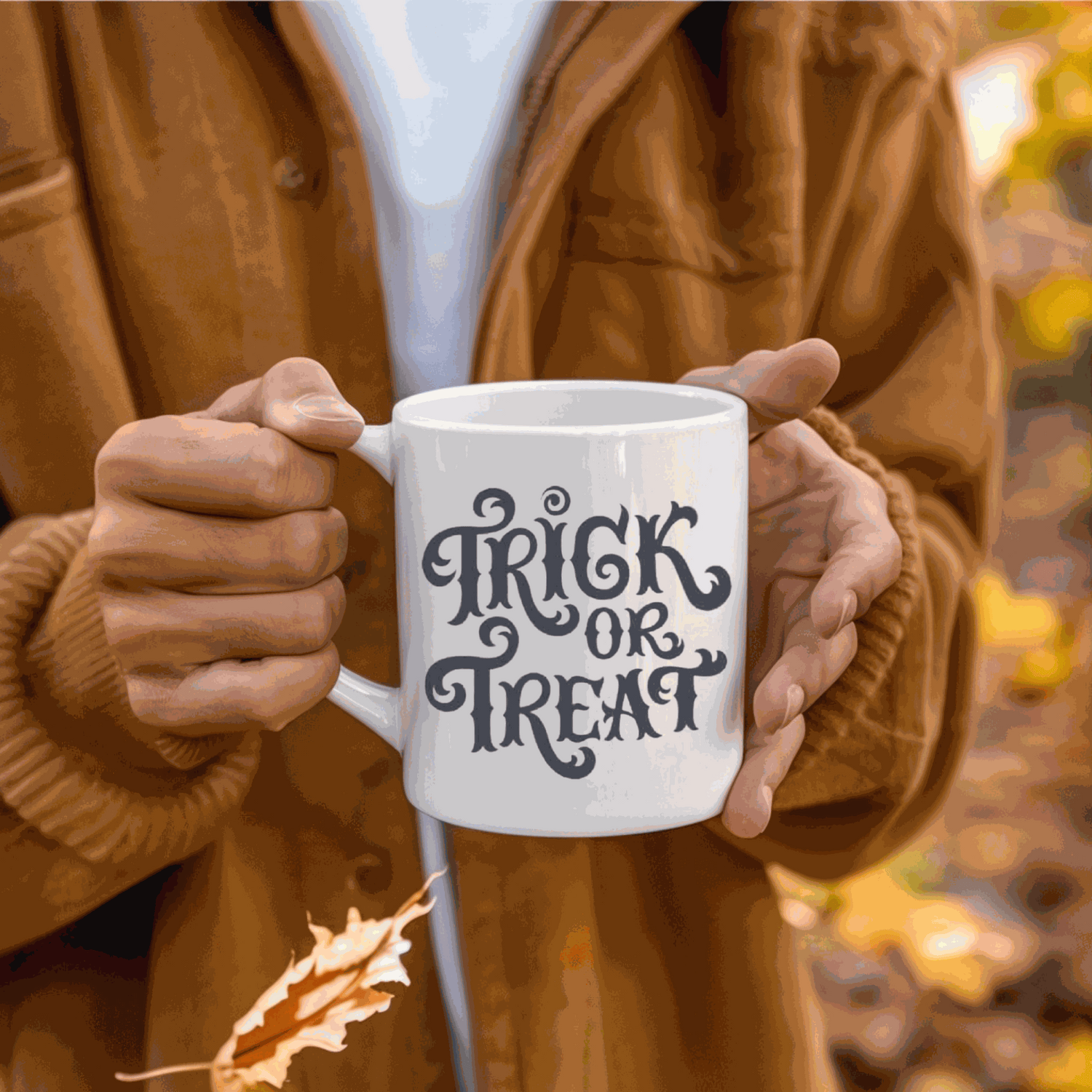 Halloween-themed ceramic mug with "Trick or Treat" design held by person in autumn setting.