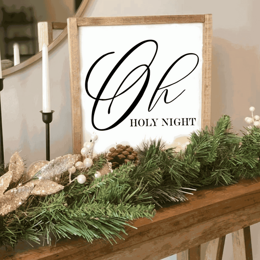 Oh Holy Night Christmas wood sign with white background and black lettering, framed with stained wood, decorated with greenery and candles.