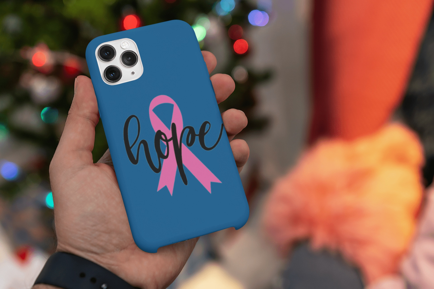 Hand holding phone with blue case featuring pink ribbon vinyl sticker and word hope in black cursive letters