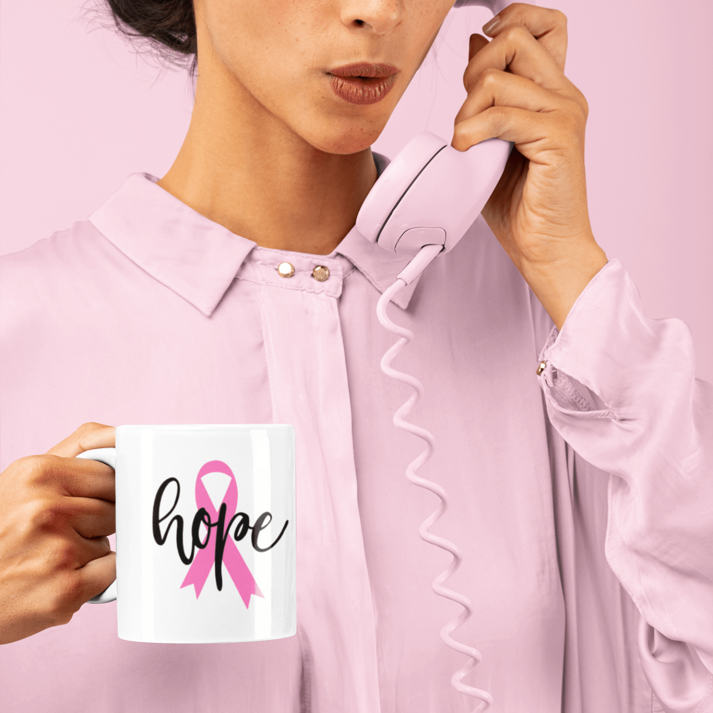Woman holding a Pink Ribbon Cancer Awareness Mug with "hope" text and a pink phone receiver against a pink background
