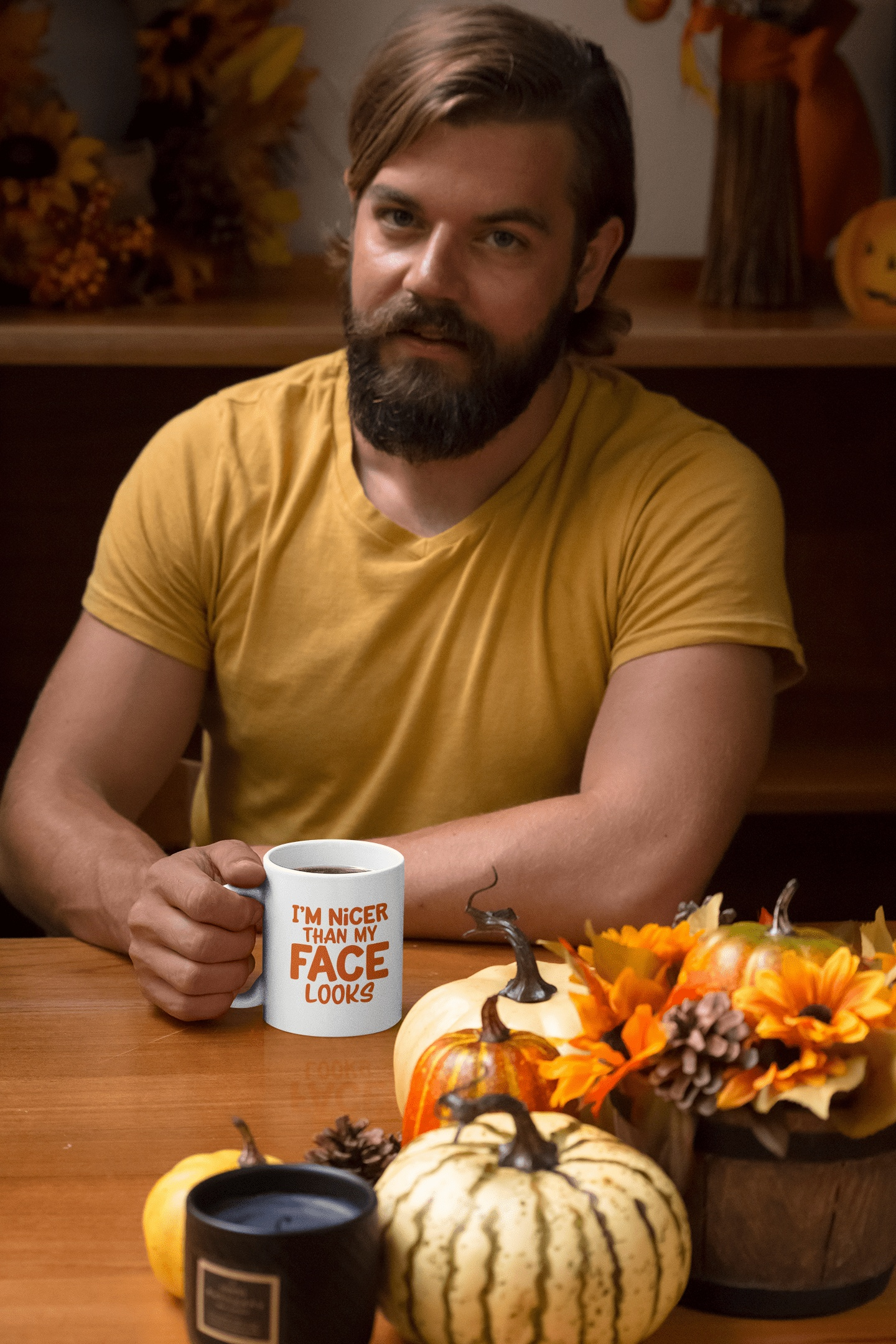 Man holding "I'm Nicer Than My Face Looks" ceramic mug with autumn decorations on table