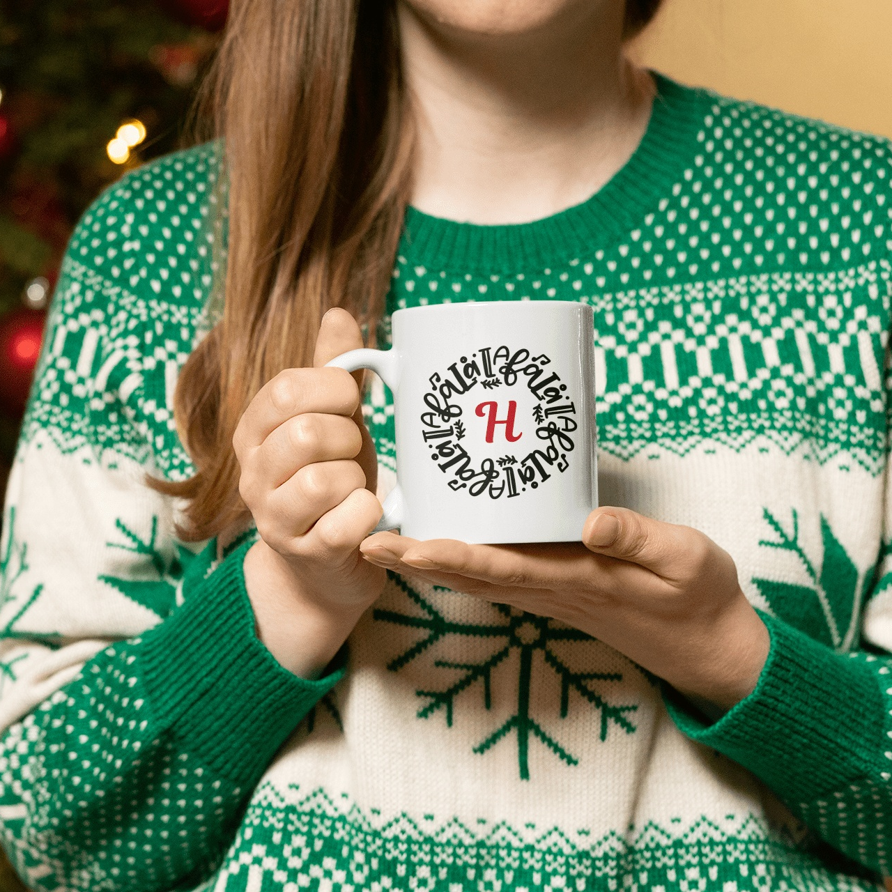 Woman holding personalized Christmas mug near tree, initial H design, festive sweater.