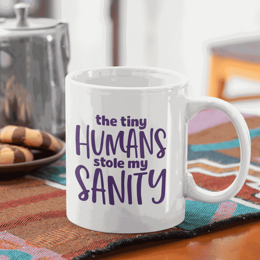 Ceramic mug with the quote "The Tiny Humans Stole my Sanity" in purple lettering, ideal for new parents.