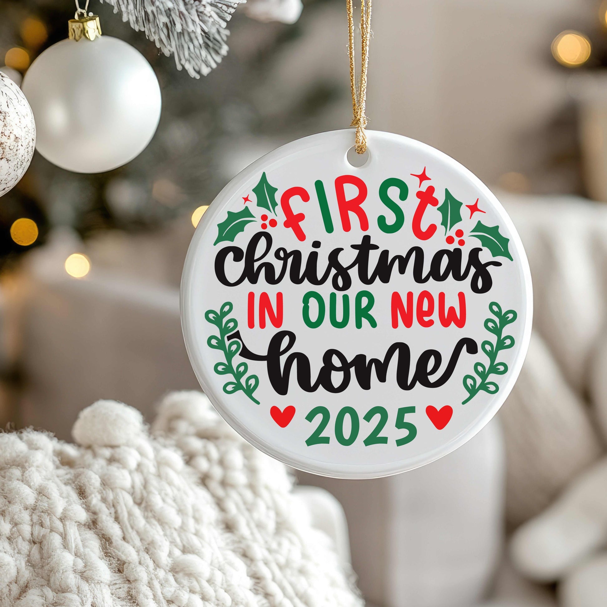 Round ceramic Christmas ornament with "First Christmas in Our New Home 2025" personalized text and holly design hanging by gold string