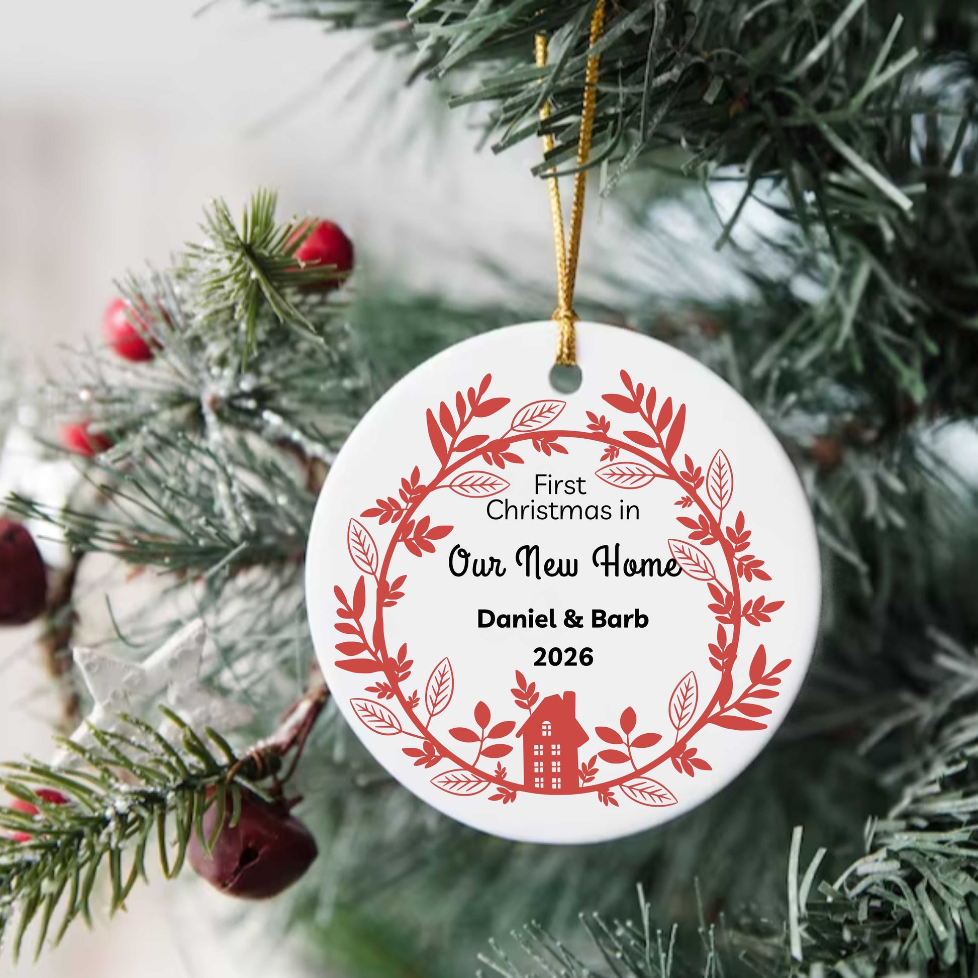 Personalized ceramic Christmas ornament with red wreath design and "First Christmas in Our New Home" text hanging on tree with gold string