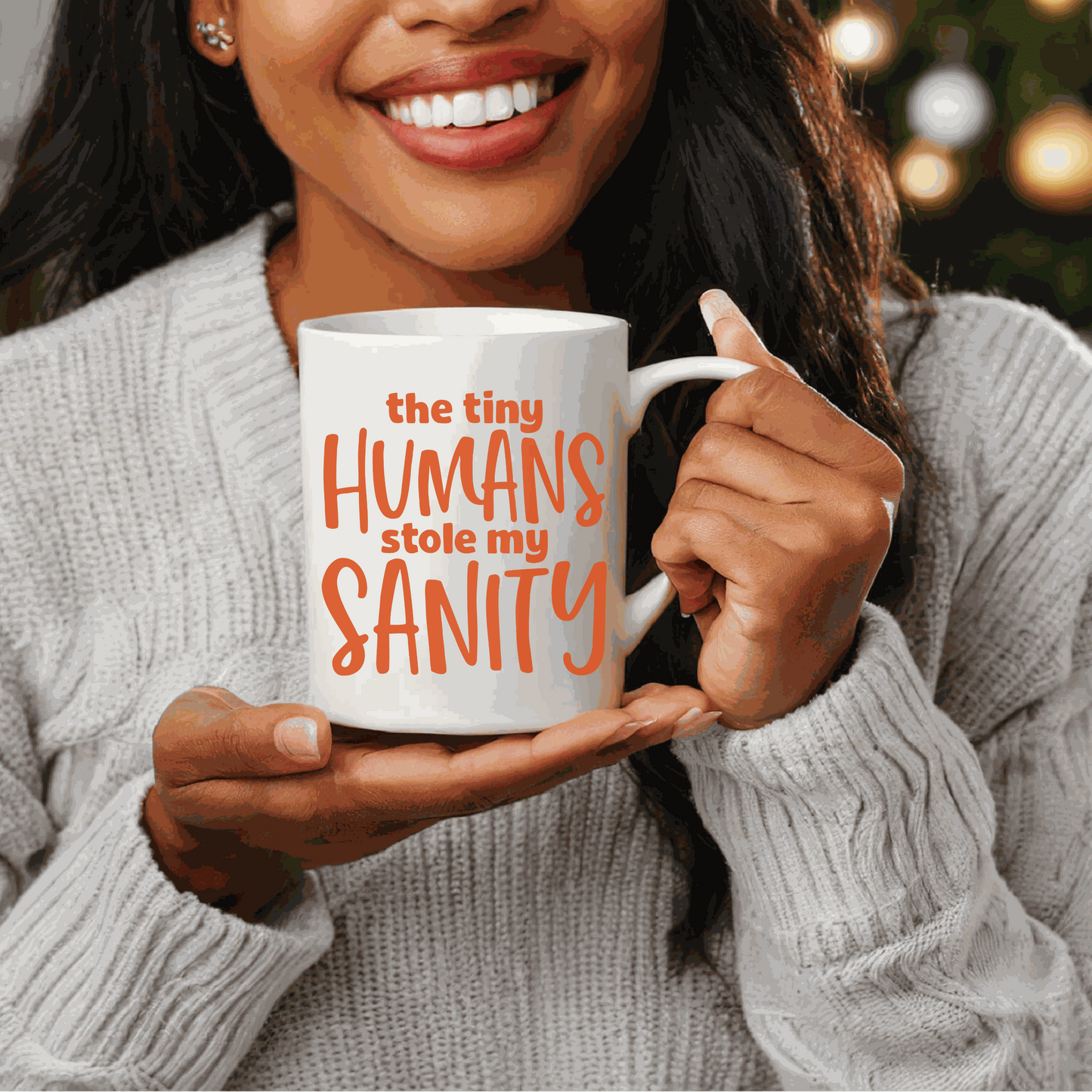 Ceramic mug with "The Tiny Humans Stole my Sanity" text, held by a smiling person wearing a gray sweater.