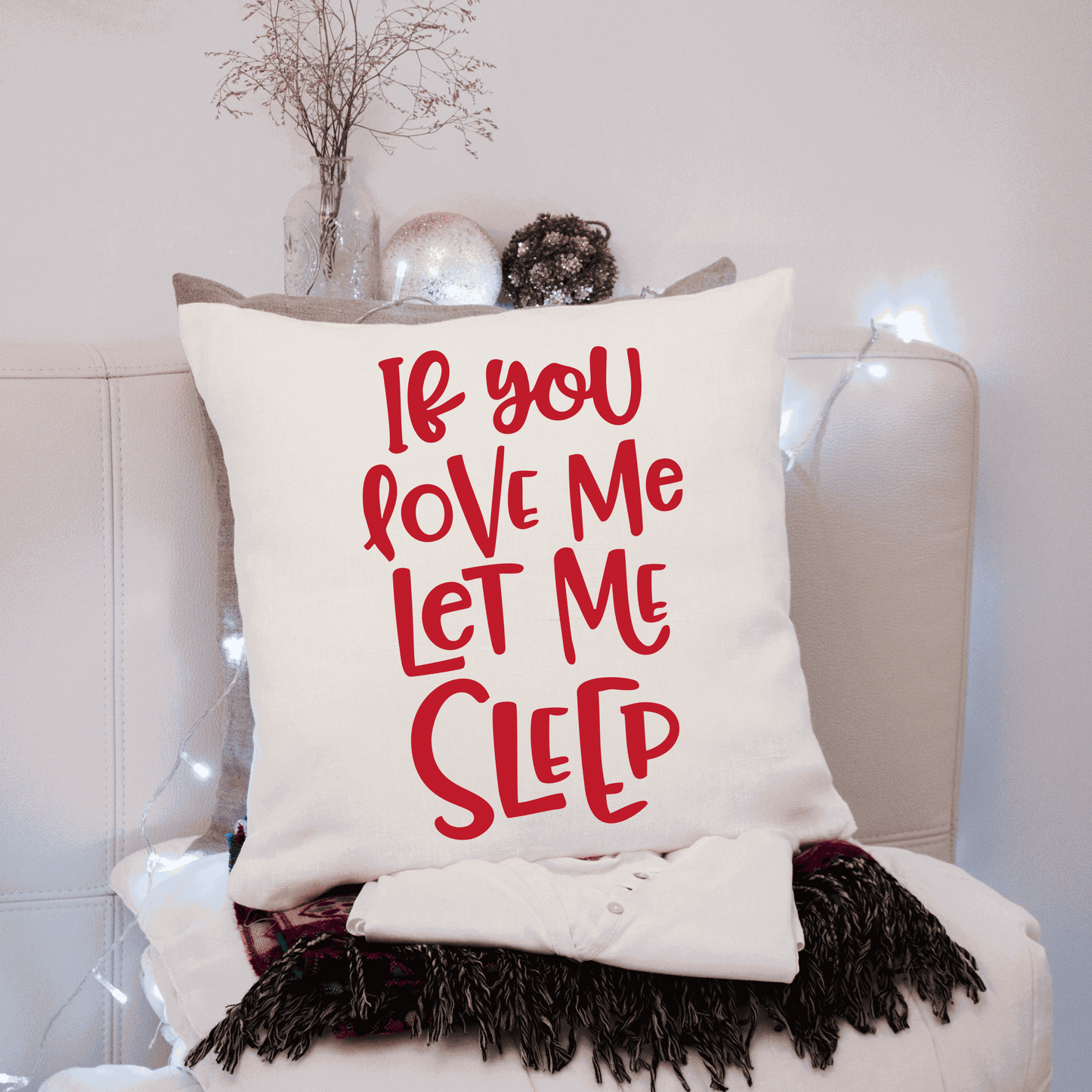 Humorous cotton pillow cover with "If You Love Me Let Me Sleep" text in red, on a cozy sofa setting.