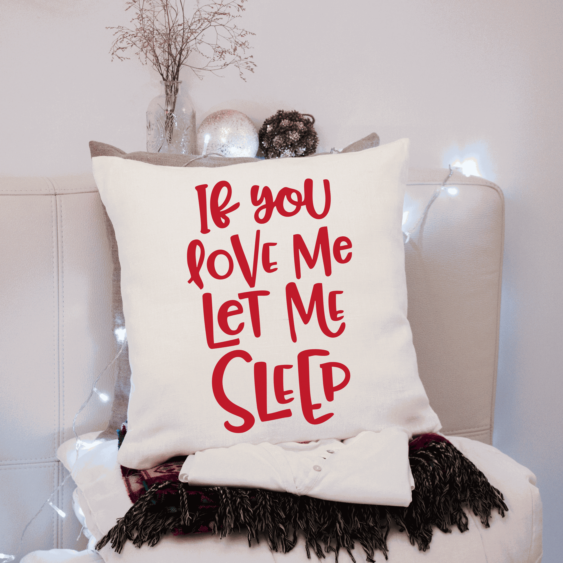 Humorous cotton pillow cover with "If You Love Me Let Me Sleep" text in red, on a cozy sofa setting.