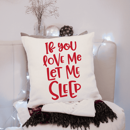 Humorous cotton pillow cover with "If You Love Me Let Me Sleep" text in red, on a cozy sofa setting.