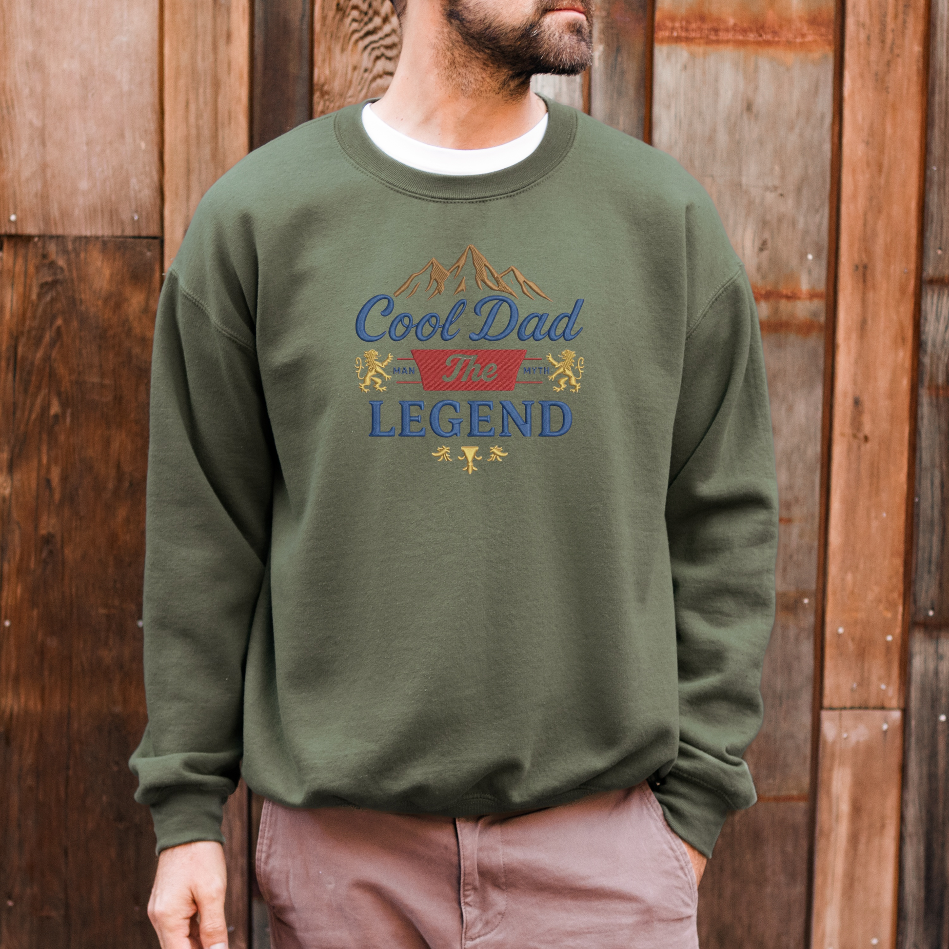 Person wearing a green sweatshirt with 'Cool Dad The Legend' text and graphics against a wooden background
