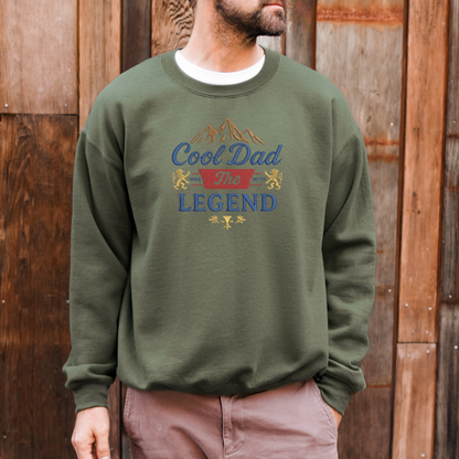 Person wearing a green sweatshirt with 'Cool Dad The Legend' text and graphics against a wooden background