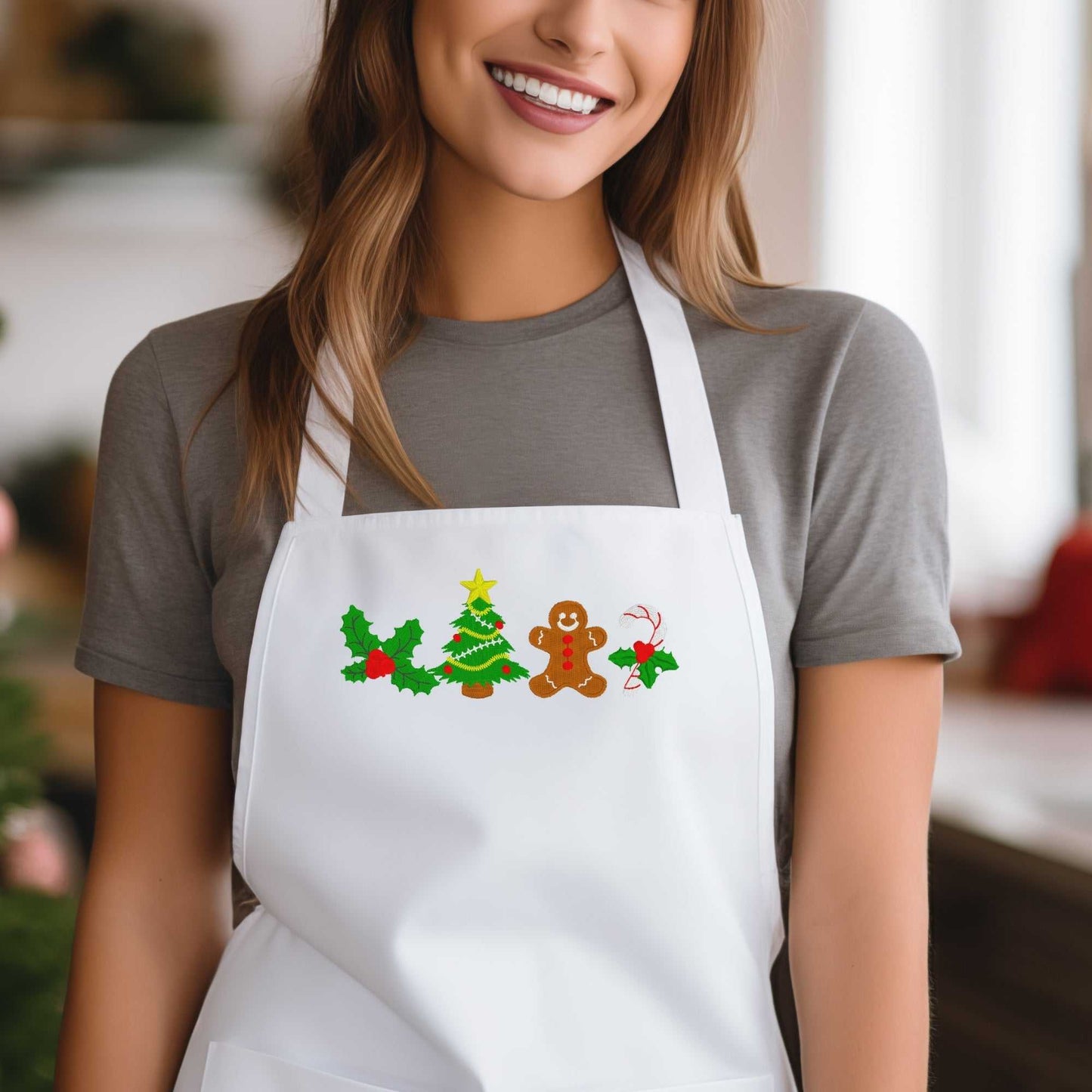 Woman wearing a white apron embroidered with festive Christmas designs including a gingerbread man, holly leaves, and a Christmas tree — a handmade holiday gift for women who love to bake.