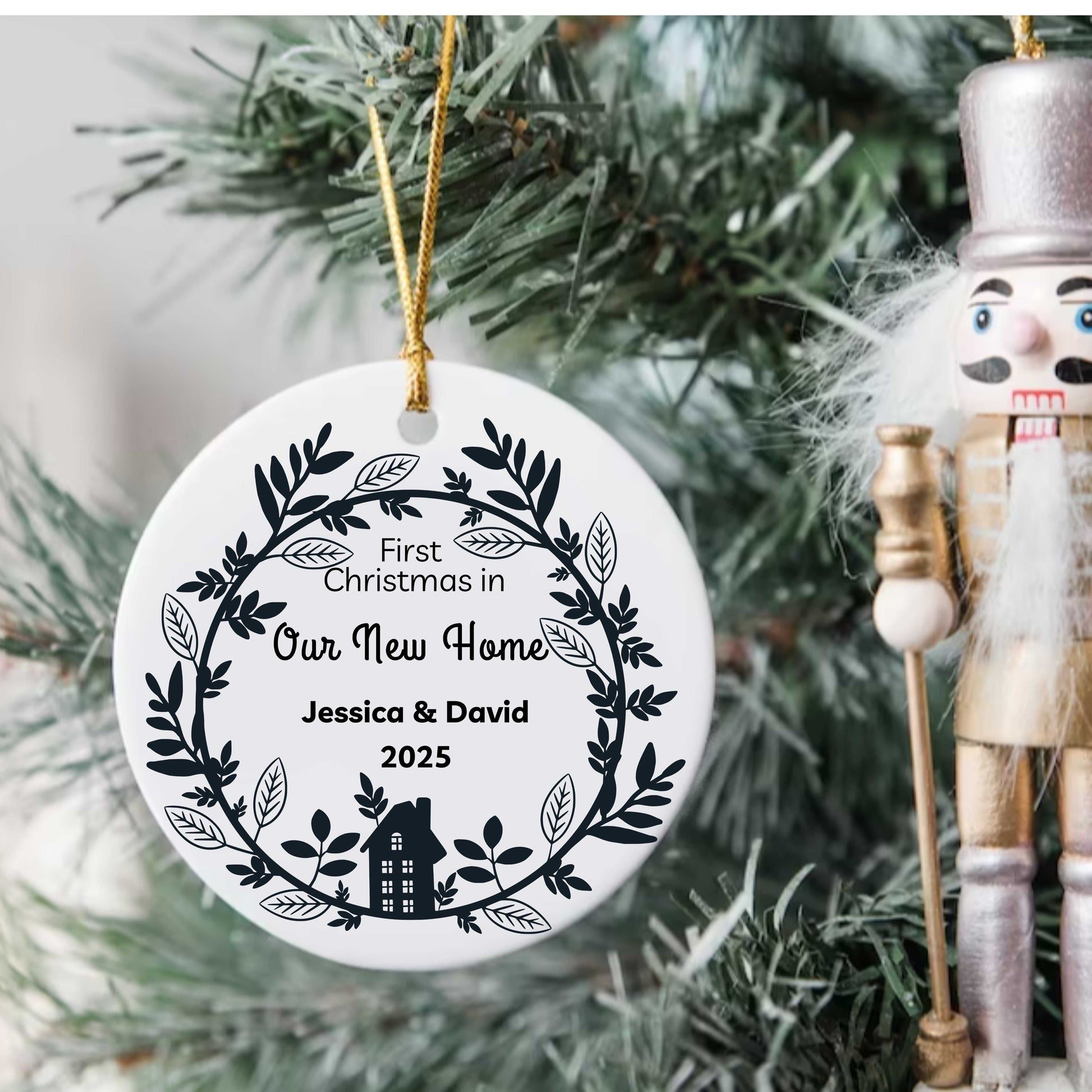 Personalized ceramic Christmas ornament for first holiday in new home with names Jessica & David 2025 hanging on tree with nutcracker nearby