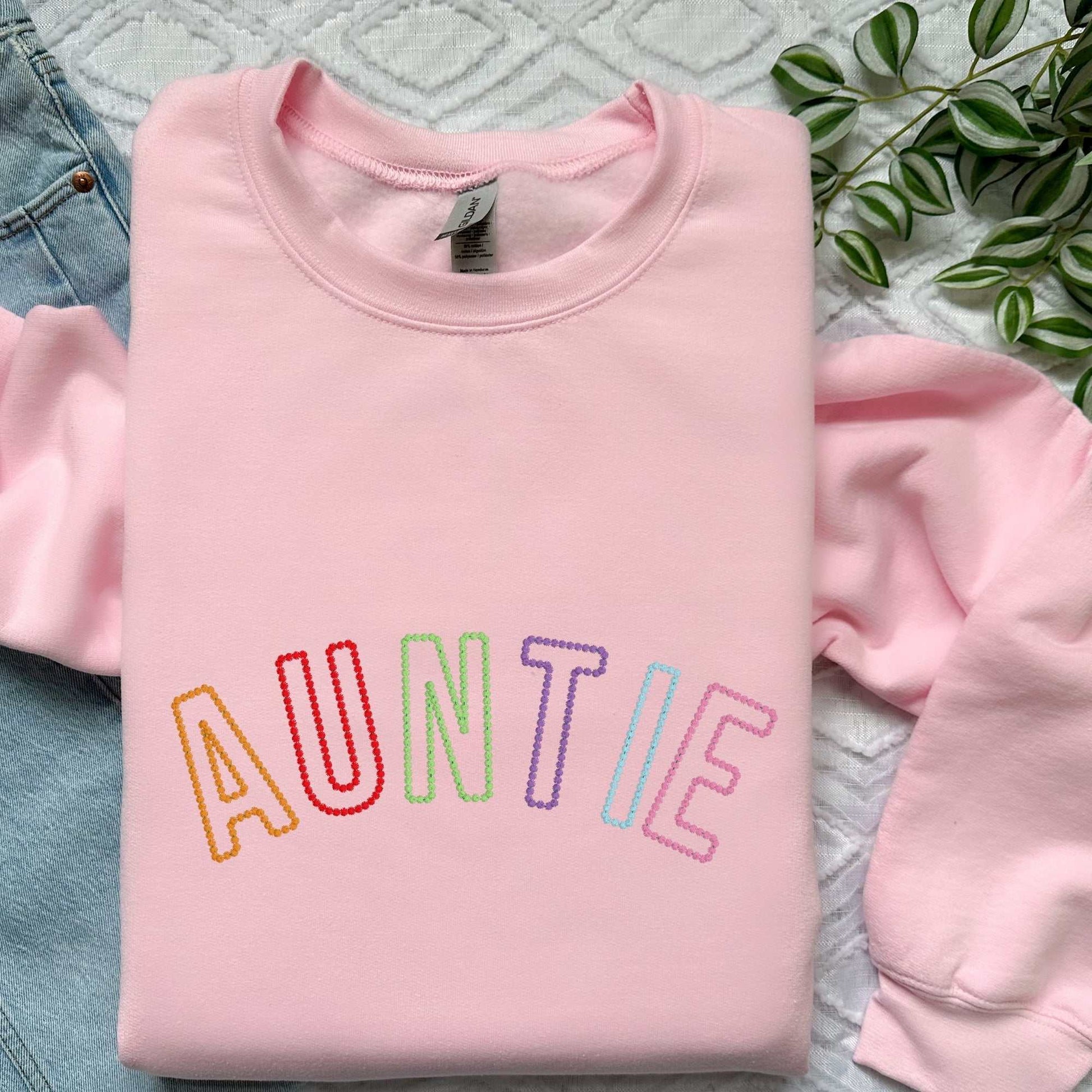 Pink sweatshirt with rainbow embroidered "AUNTIE" letters, soft cotton blend, unisex fit.