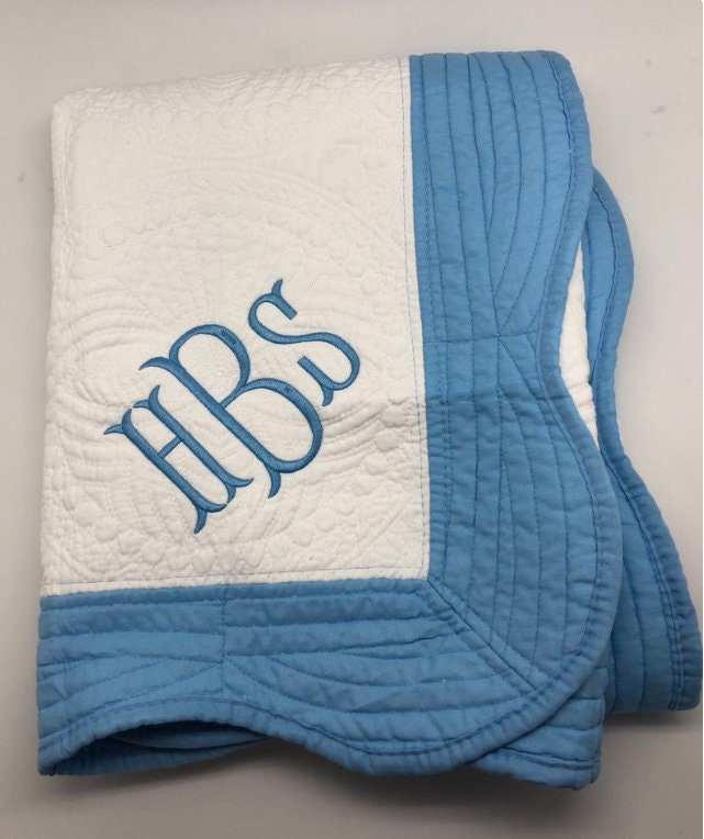 Personalized embroidered baby blanket with blue trim, featuring a custom monogram design.