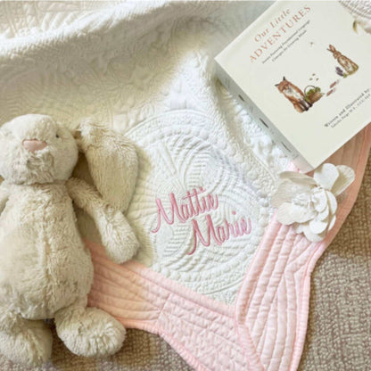 Personalized embroidered baby blanket with pink trim, featuring name "Mattie Marie", soft plush toy, and children's book.
