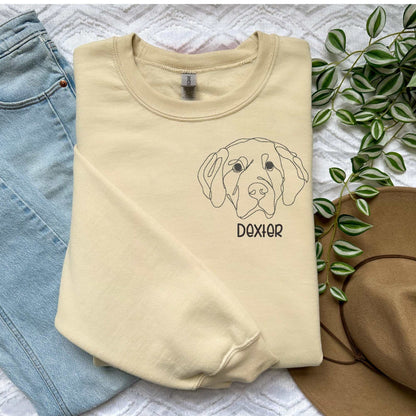 Cream classic crewneck sweater with embroidered Golden Retriever dog face and name "Dexter" in block font, styled with light blue jeans and brown hat