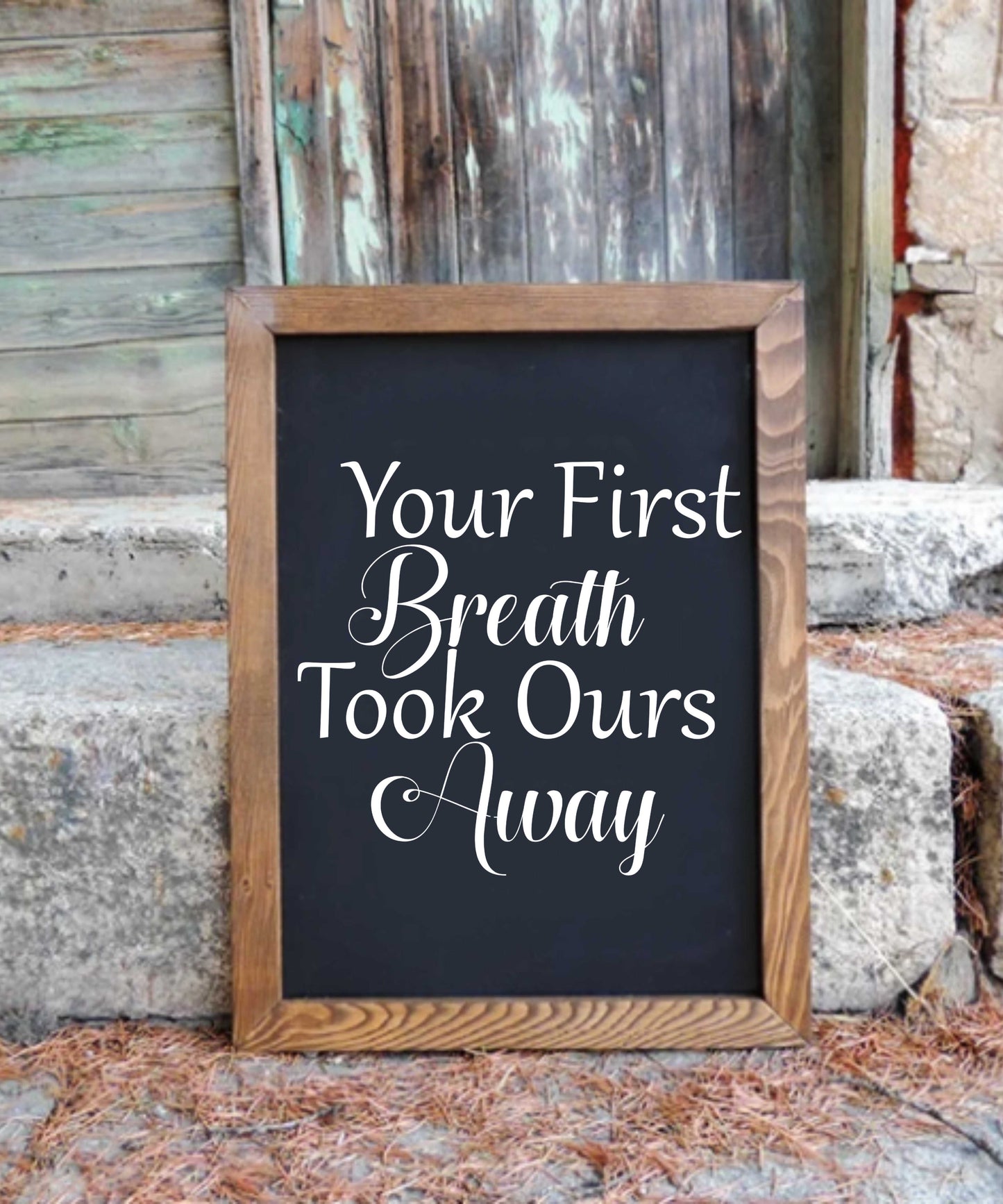 Wood framed sign with black background and white lettering reading "Your First Breath Took Ours Away" for nursery décor