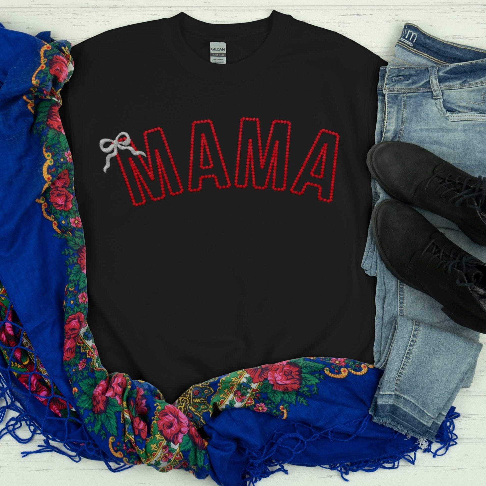 Custom embroidered "MAMA" sweatshirt with red stitched text and bow detail, displayed with jeans and colorful scarf.