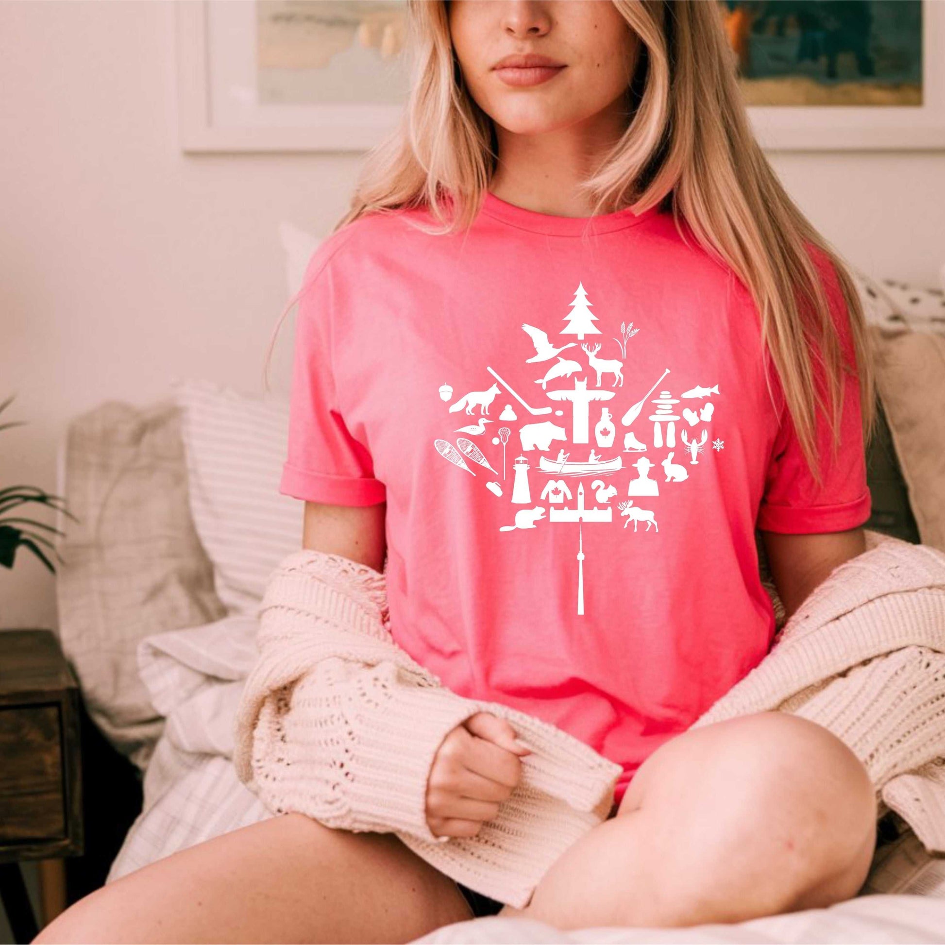 Unisex red maple leaf t-shirt featuring iconic Canadian imagery, worn by a woman sitting indoors.