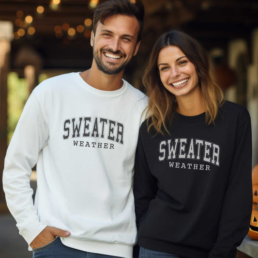 Smiling man and woman wearing embroidered "Sweater Weather" crewneck sweatshirts in white and black, cozy