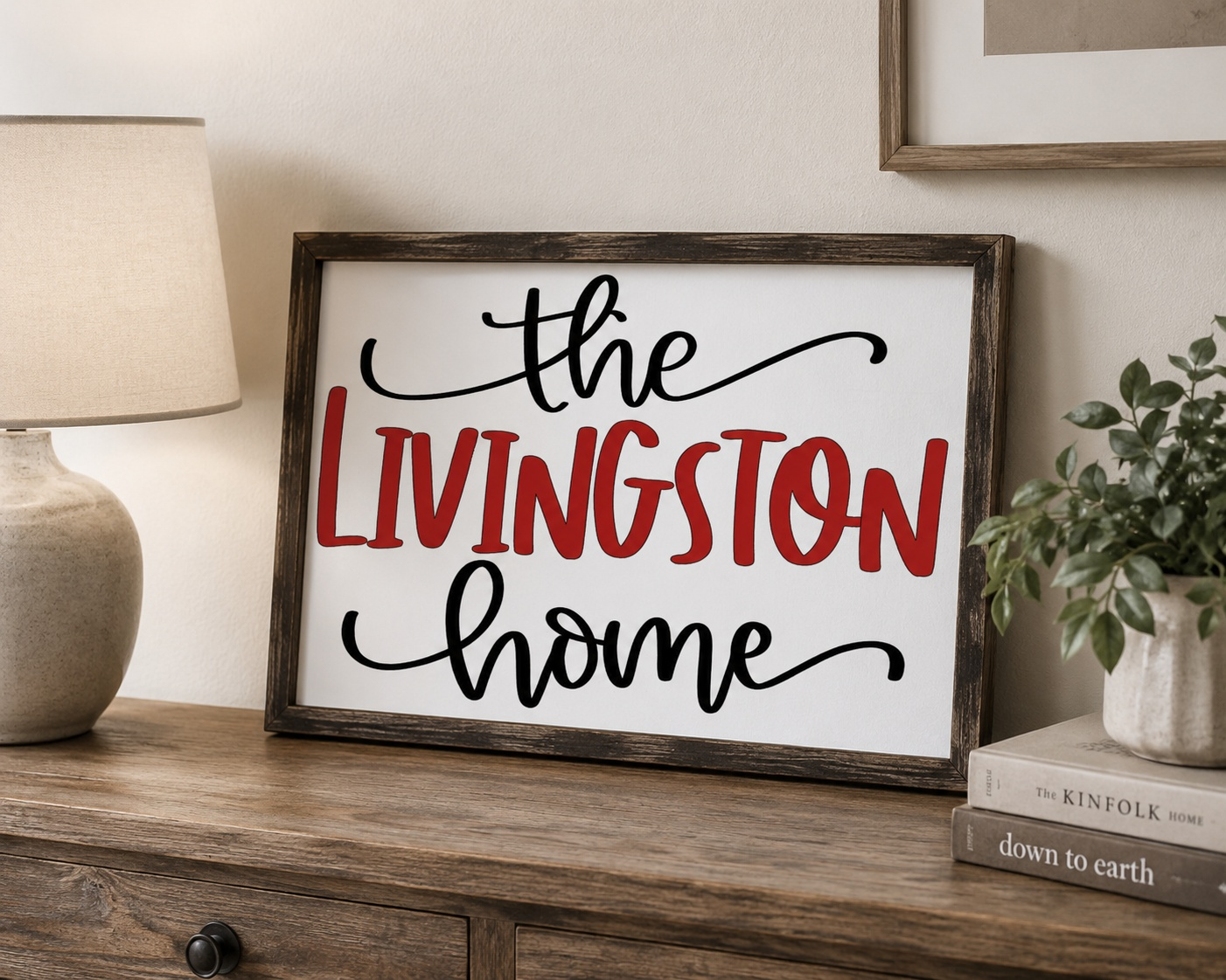 Decorative sign with 'the Livingston home' on a wooden surface with a lamp and plant in the background.