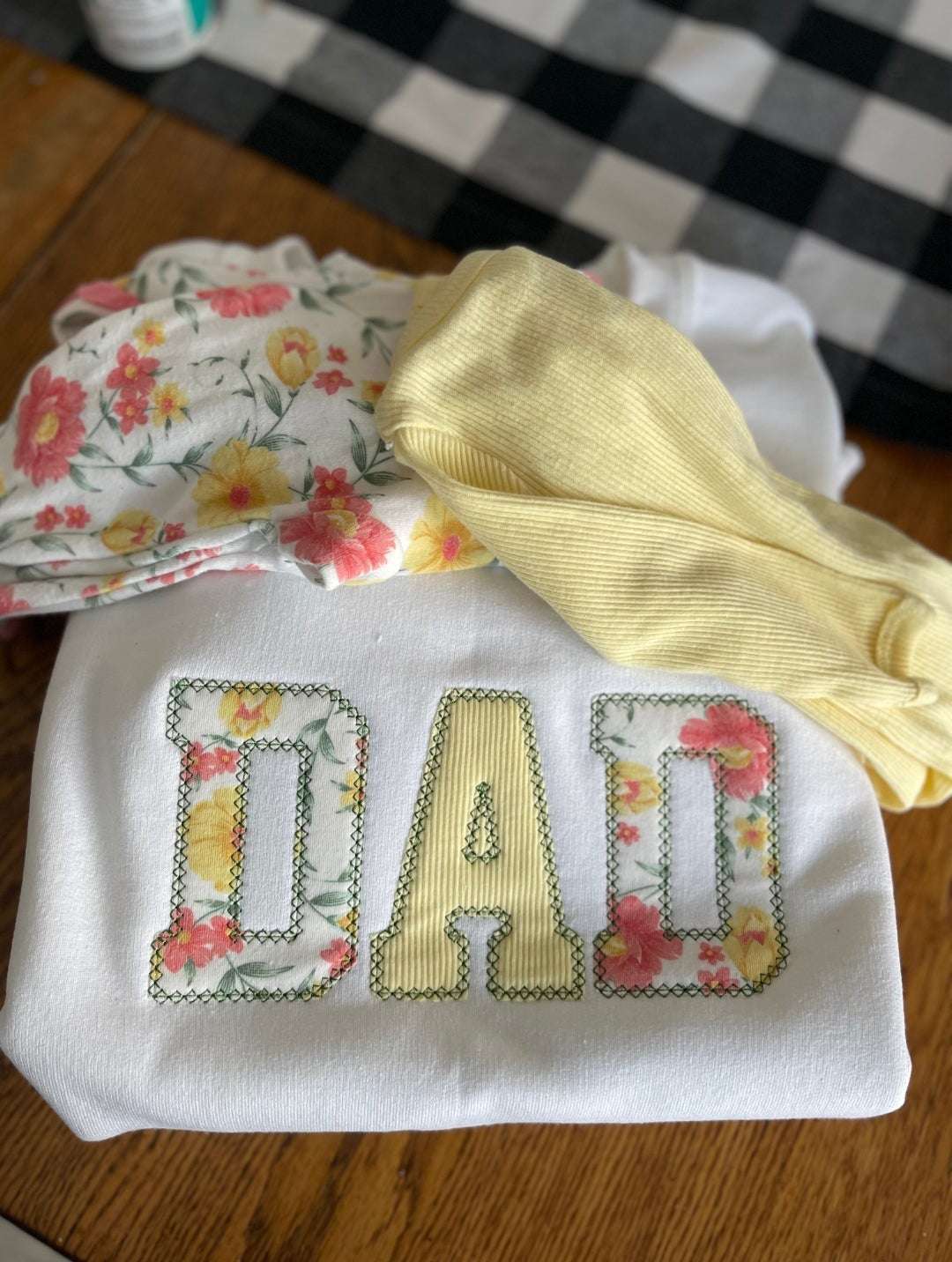 White sweater with floral and yellow fabric patches forming the word "DAD" as a meaningful keepsake from clothes