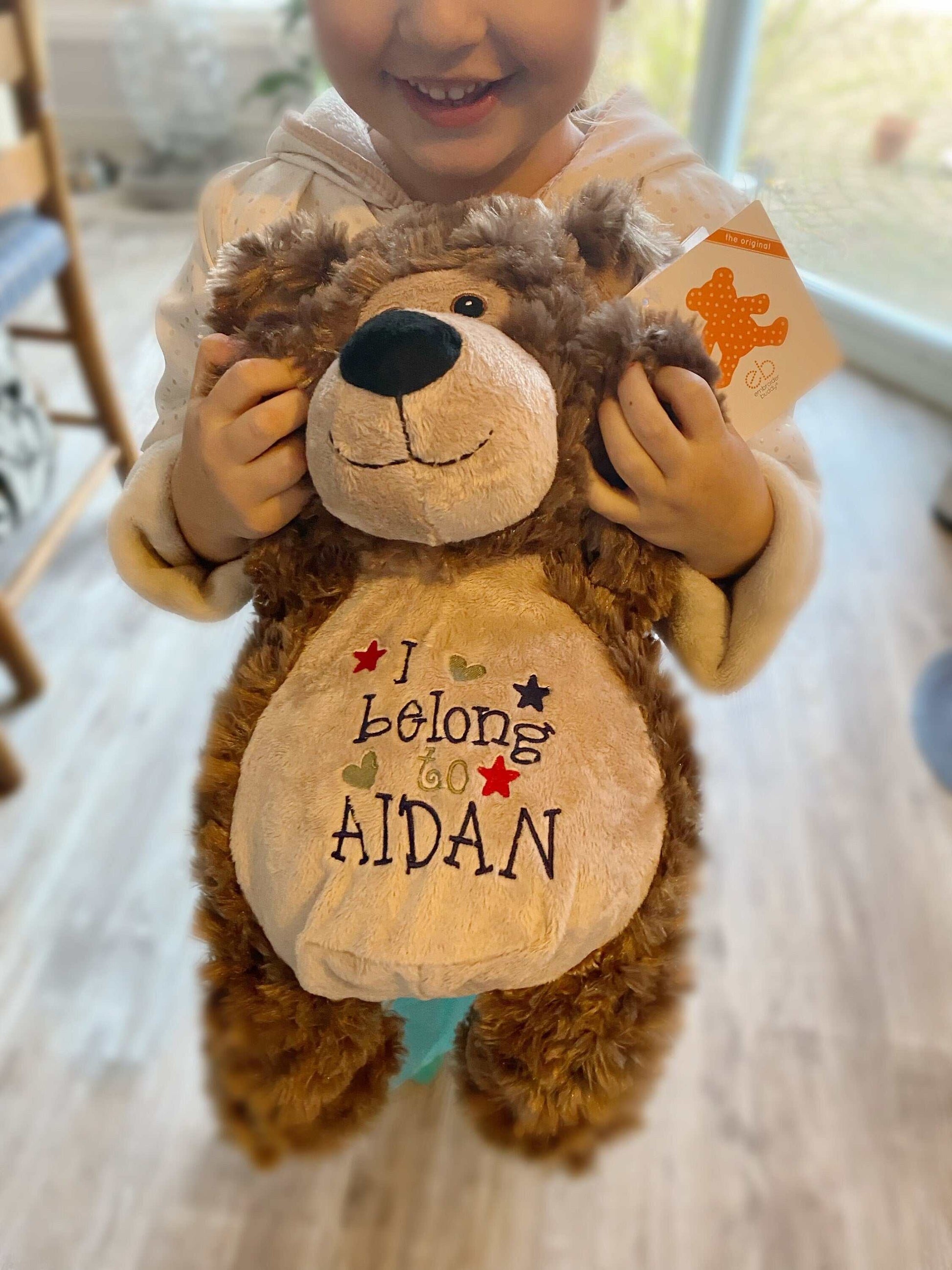 Personalized stuffed bear with embroidered "I Belong to" design held by child.