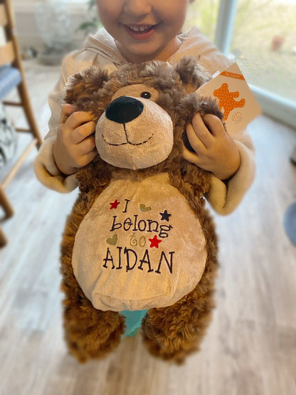 Personalized stuffed bear with embroidered "I Belong to" design held by child.