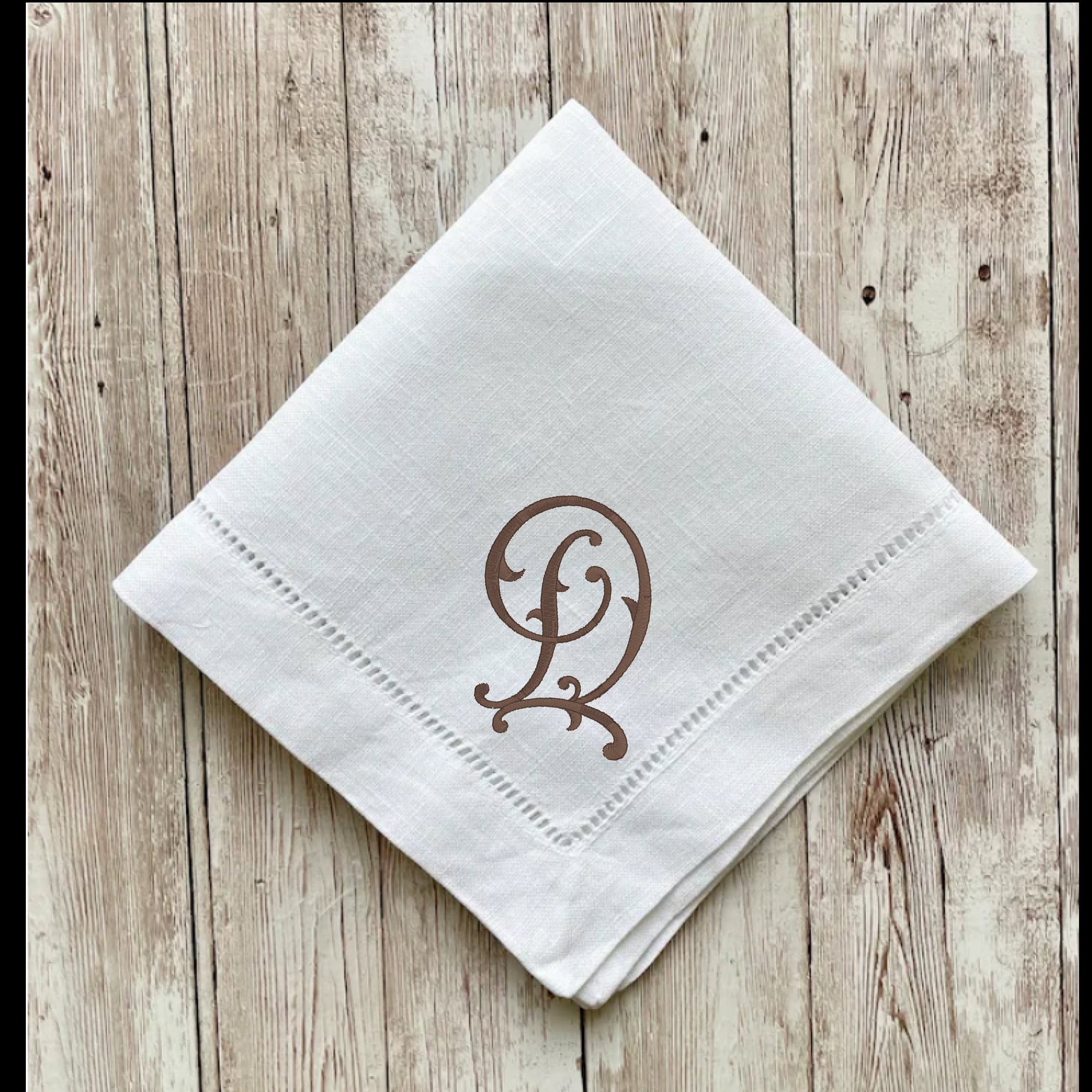White napkin with brown monogram on a wooden surface