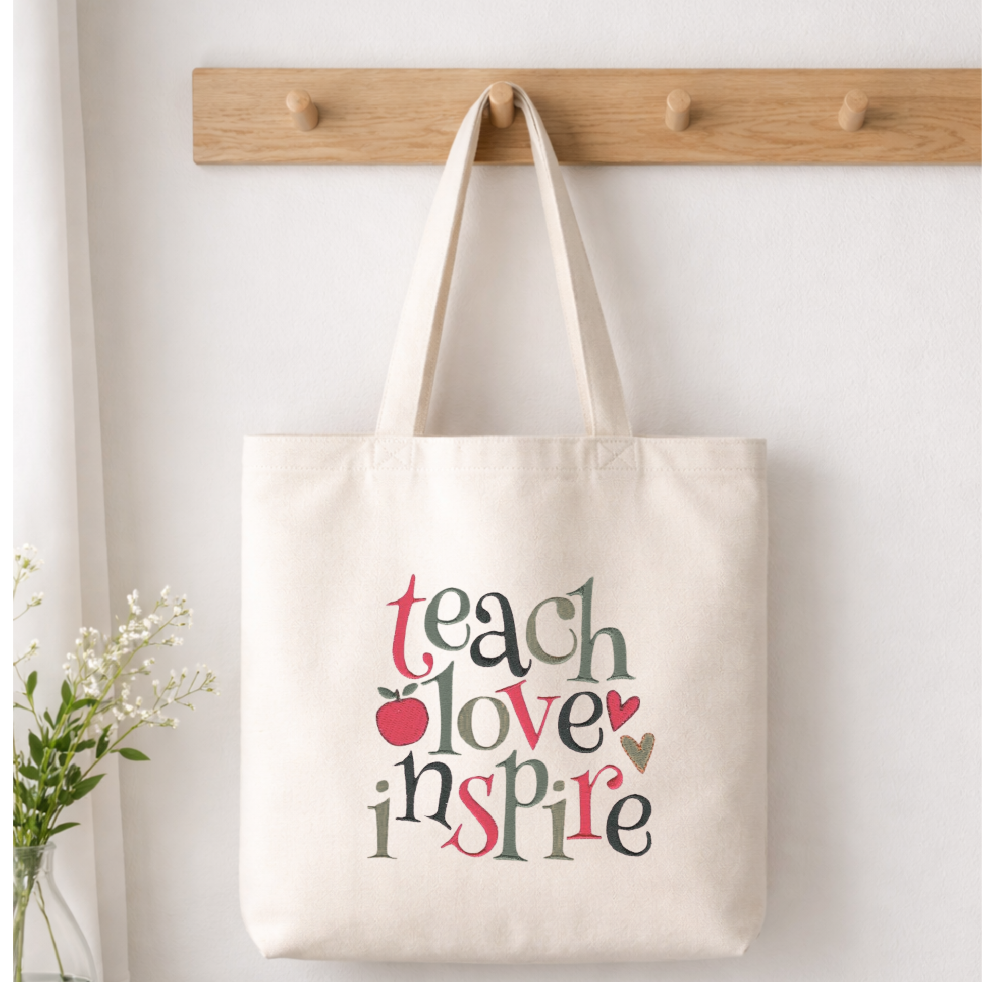 White canvas tote bag embroidered with the words Teach, Love, Inspire, perfect for educators and mentors.