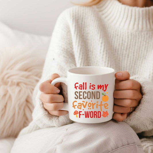 White ceramic mug with "Fall is my second favorite F-word" text in fall colors, held by person in cozy sweater