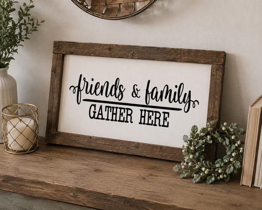 Wooden-framed sign with 'friends & family GATHER HERE' text on a wooden surface with decorative items.