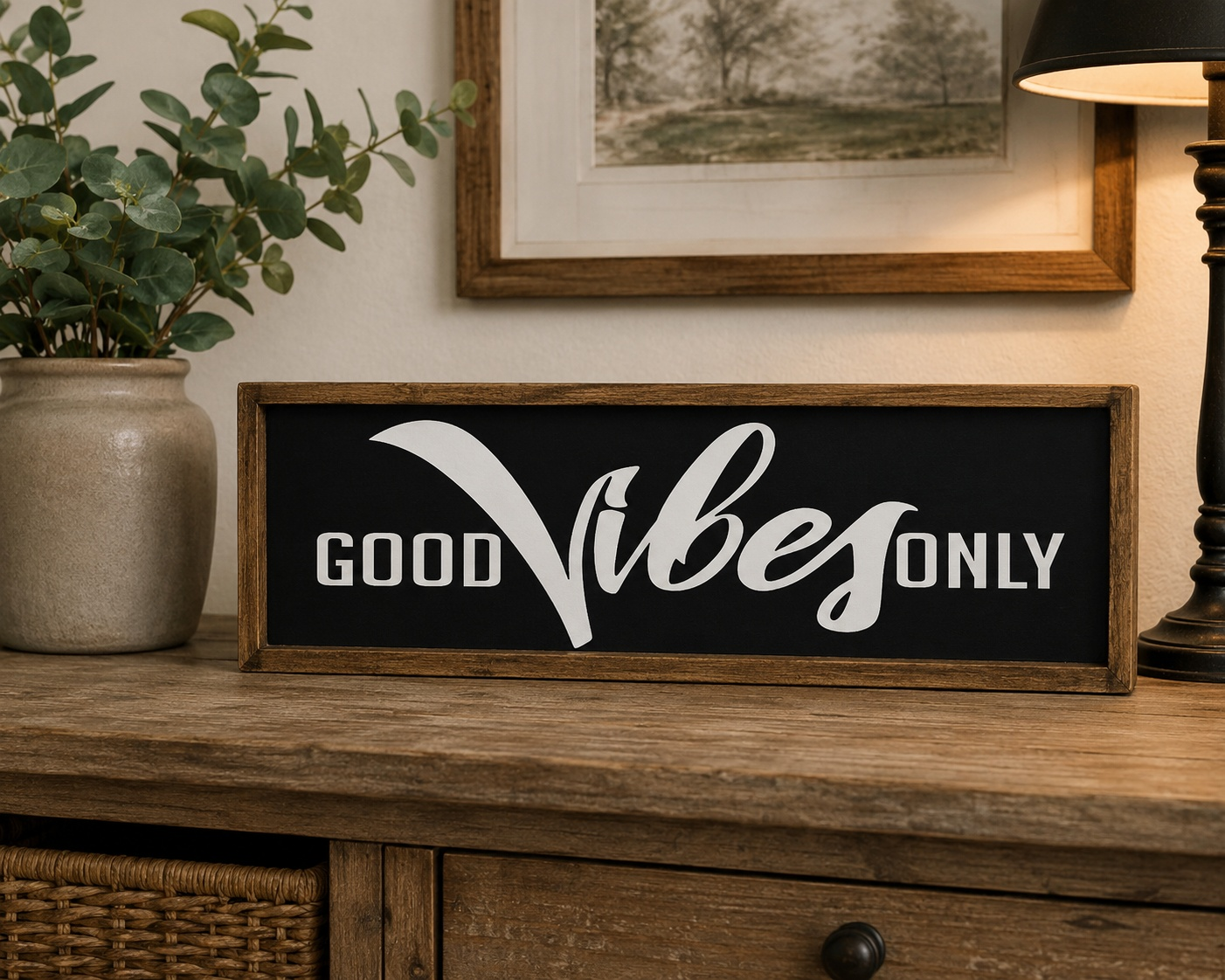 Decorative sign with 'Good Vibes Only' on a wooden surface with a plant and lamp in the background.