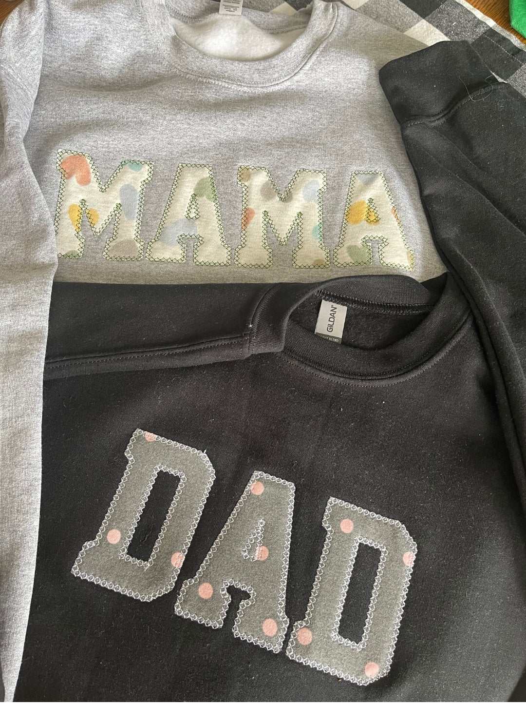 Gray sweater with floral patch letters spelling MAMA and black sweater with gray patch letters spelling DAD, meaningful keepsake clothing made from personal clothes