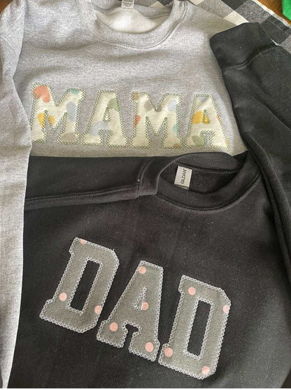 Gray sweater with floral patch letters spelling MAMA and black sweater with gray patch letters spelling DAD, meaningful keepsake clothing made from personal clothes
