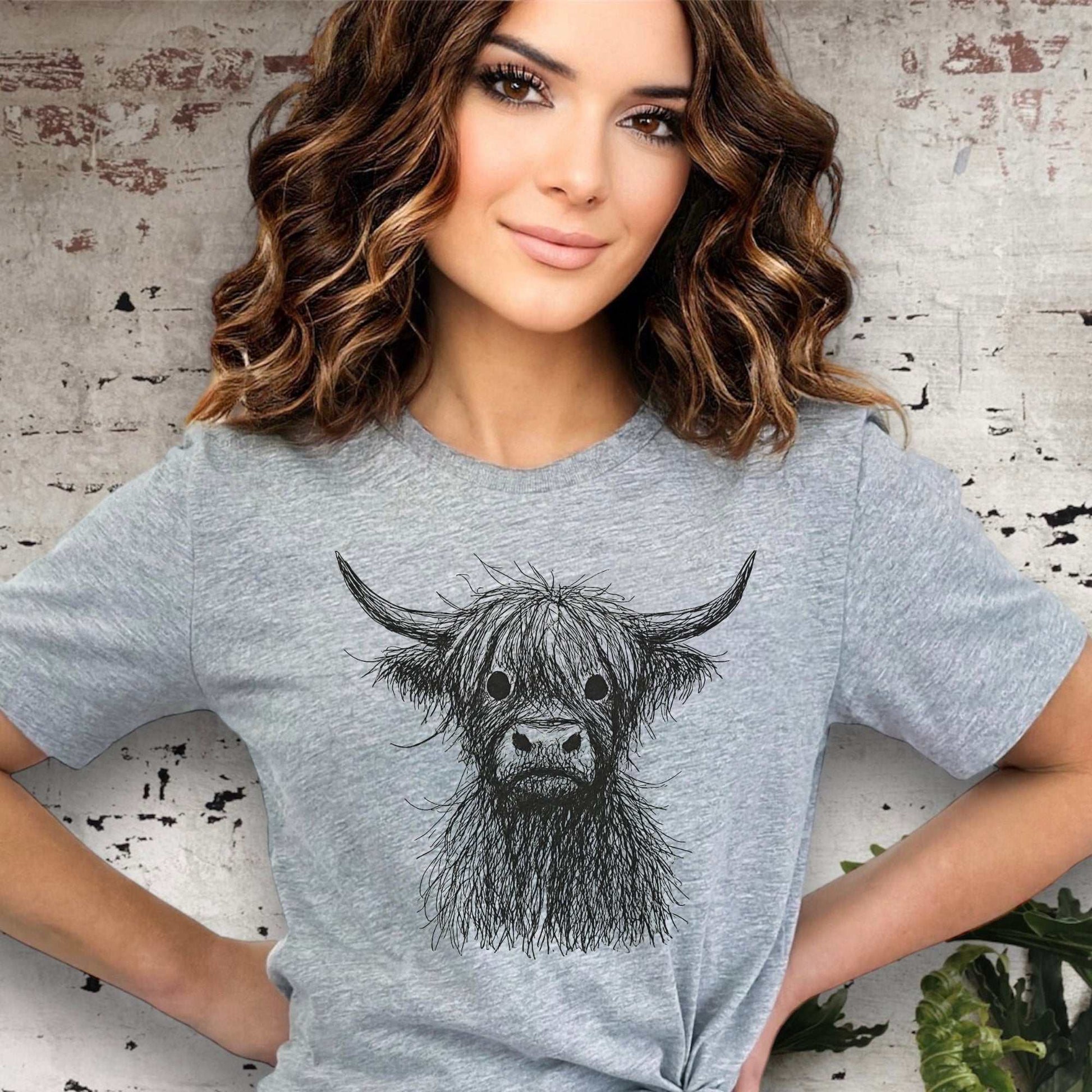 Woman wearing a gray t-shirt with a cow illustration against a textured wall background