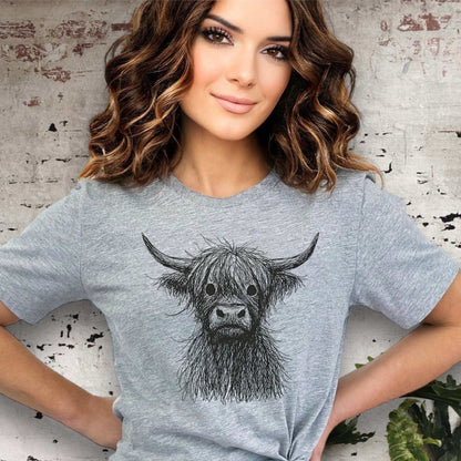 Woman wearing a gray t-shirt with a cow illustration against a textured wall background