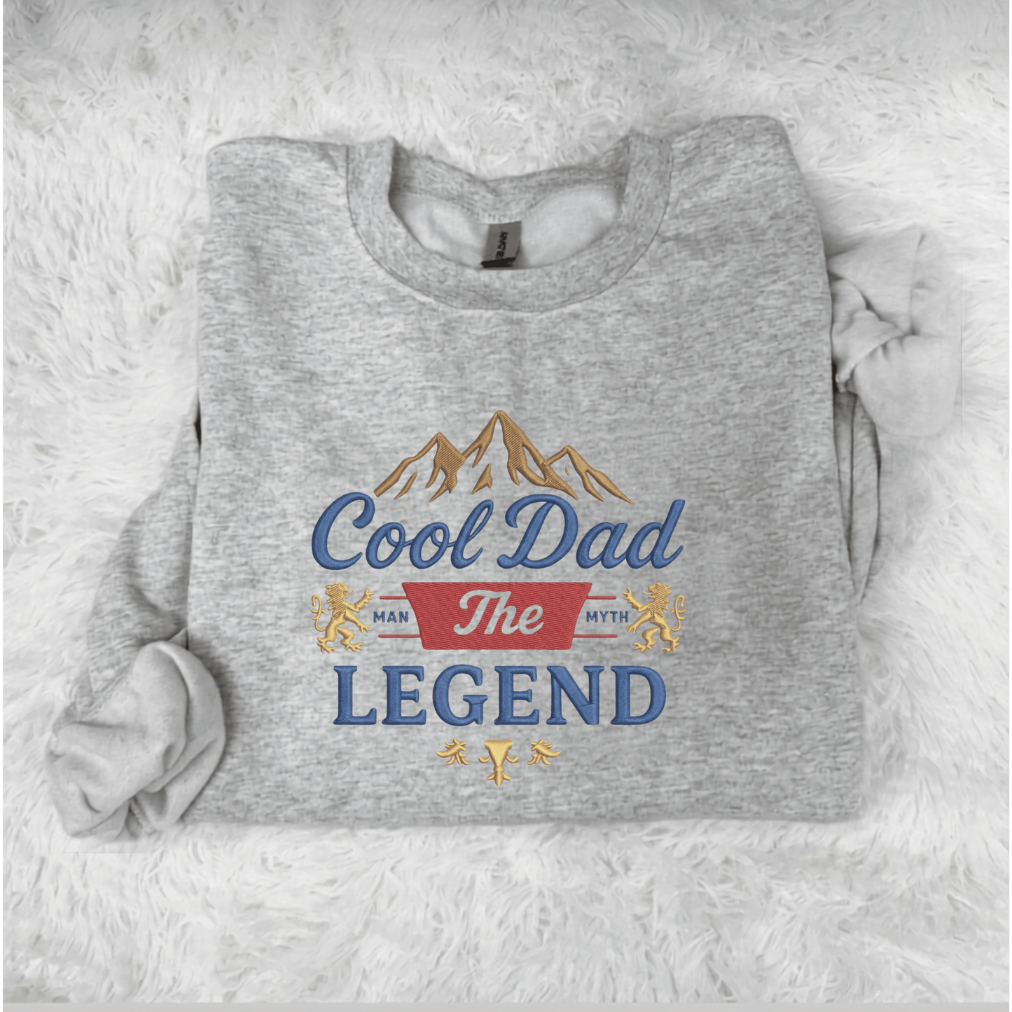 Gray sweatshirt with 'Cool Dad The Legend' text and mountain graphic on a white fluffy background