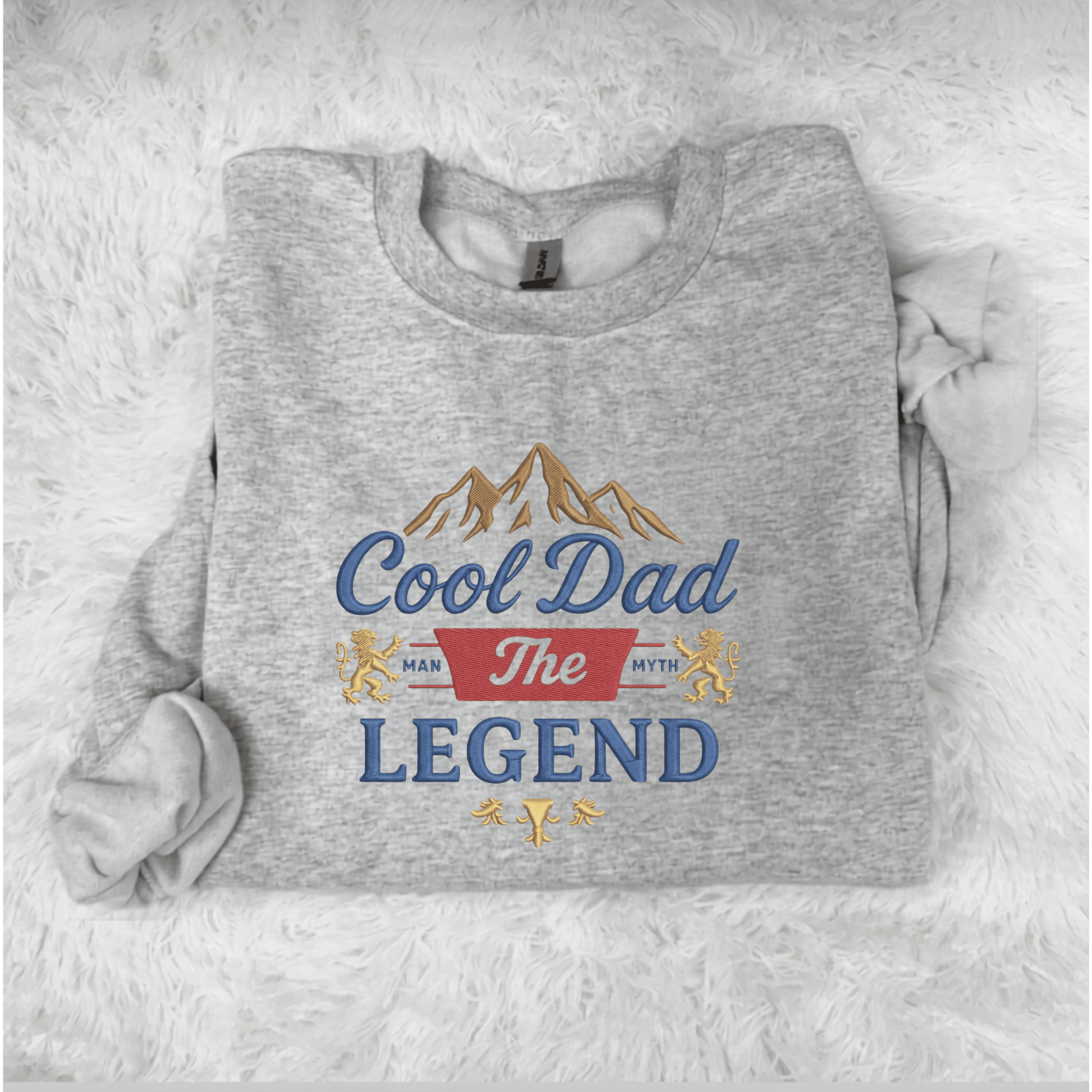 Gray sweatshirt with 'Cool Dad The Legend' text and mountain graphic on a white fluffy background