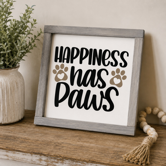 Framed sign with 'Happiness has Paws' text on a wooden surface with decorative items.