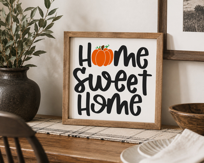 Framed sign with 'Home Sweet Home' and a pumpkin on a wooden surface.