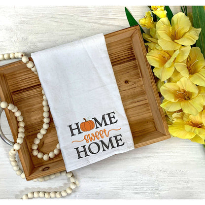 Thanksgiving themed white cotton tea towel with embroidered "Home sweet Home" and pumpkin design on wooden tray with yellow flowers