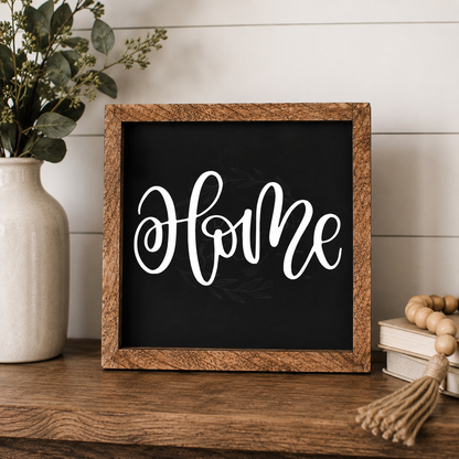 Decorative sign with 'Home' text on a wooden frame, next to a vase with greenery and books.