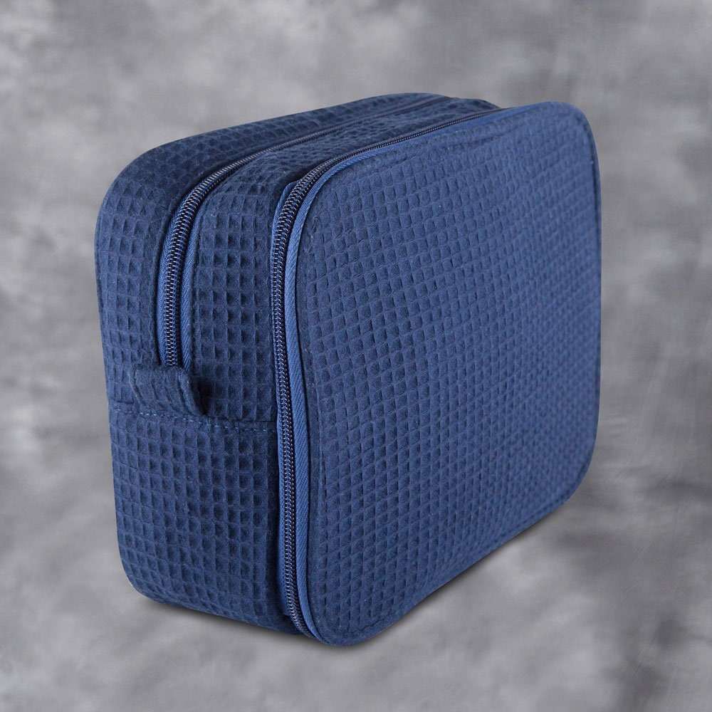 Monogrammed cosmetic bag with soft waffle texture and interior zipped compartments for makeup and toiletries storage.