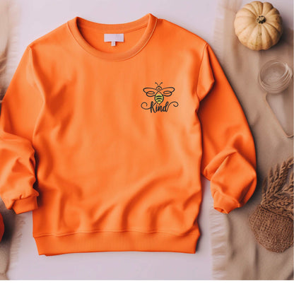 Orange embroidered "Be Kind" bumble bee sweatshirt on display with fall decor.