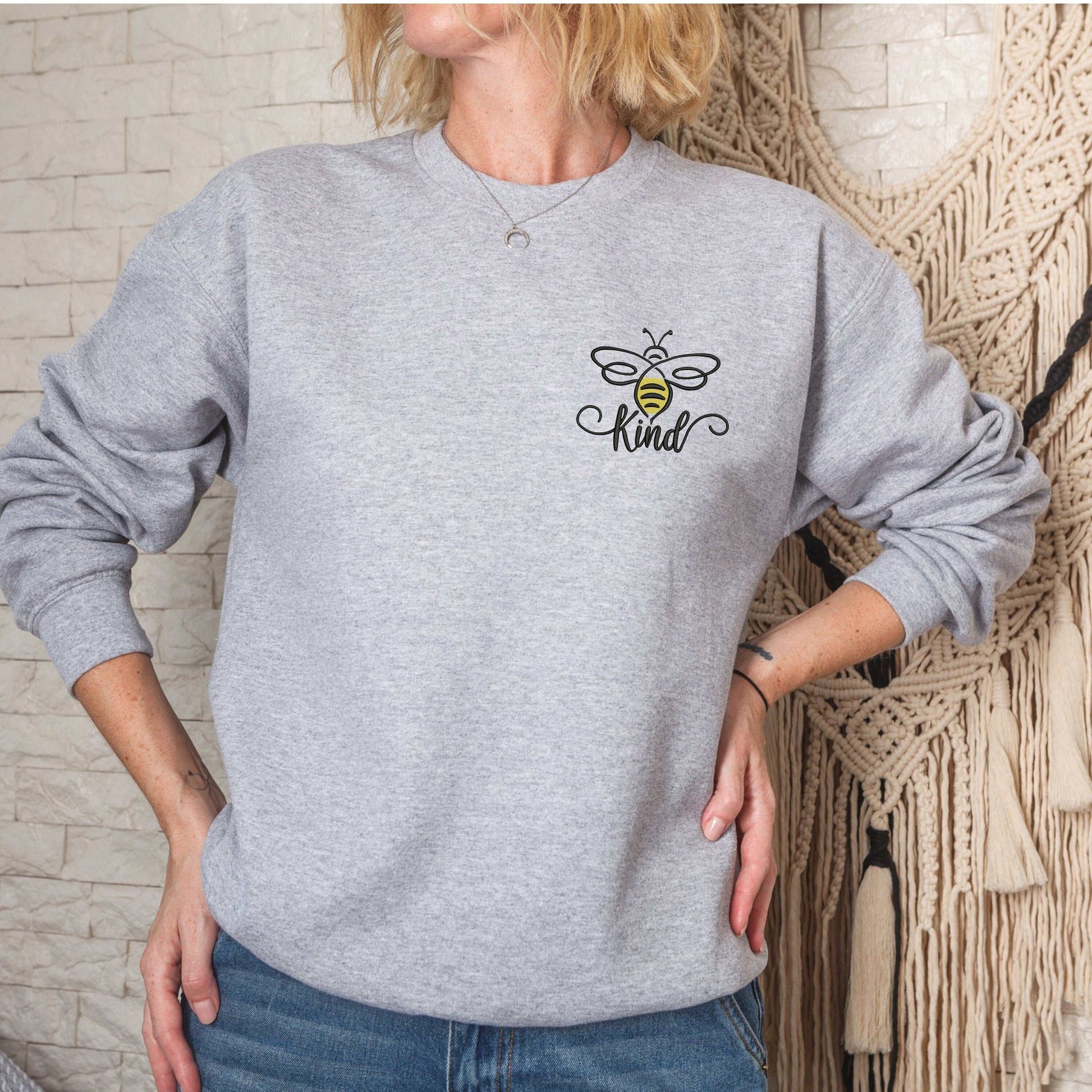 Bumble Bee Be Kind embroidered sweatshirt in gray, unisex sizing, worn by a woman with blue jeans.