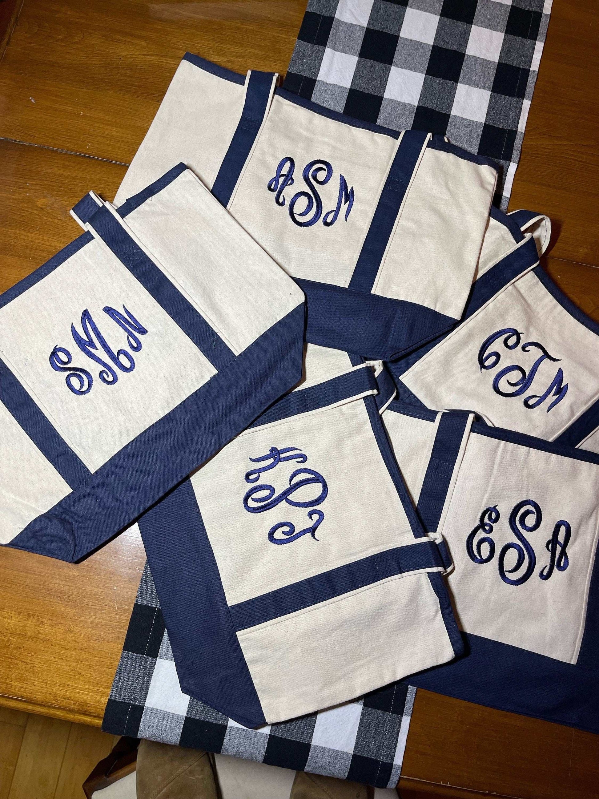 Personalized embroidered tote bags with monograms on the front pocket, featuring long handles and durable canvas material.