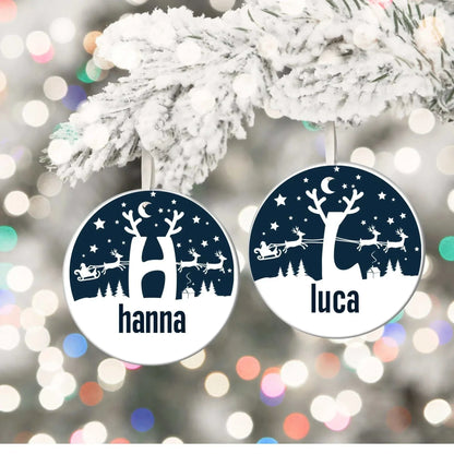 Personalized Christmas round porcelain ornaments with reindeer scene and monogram letters hanging on snowy tree branch